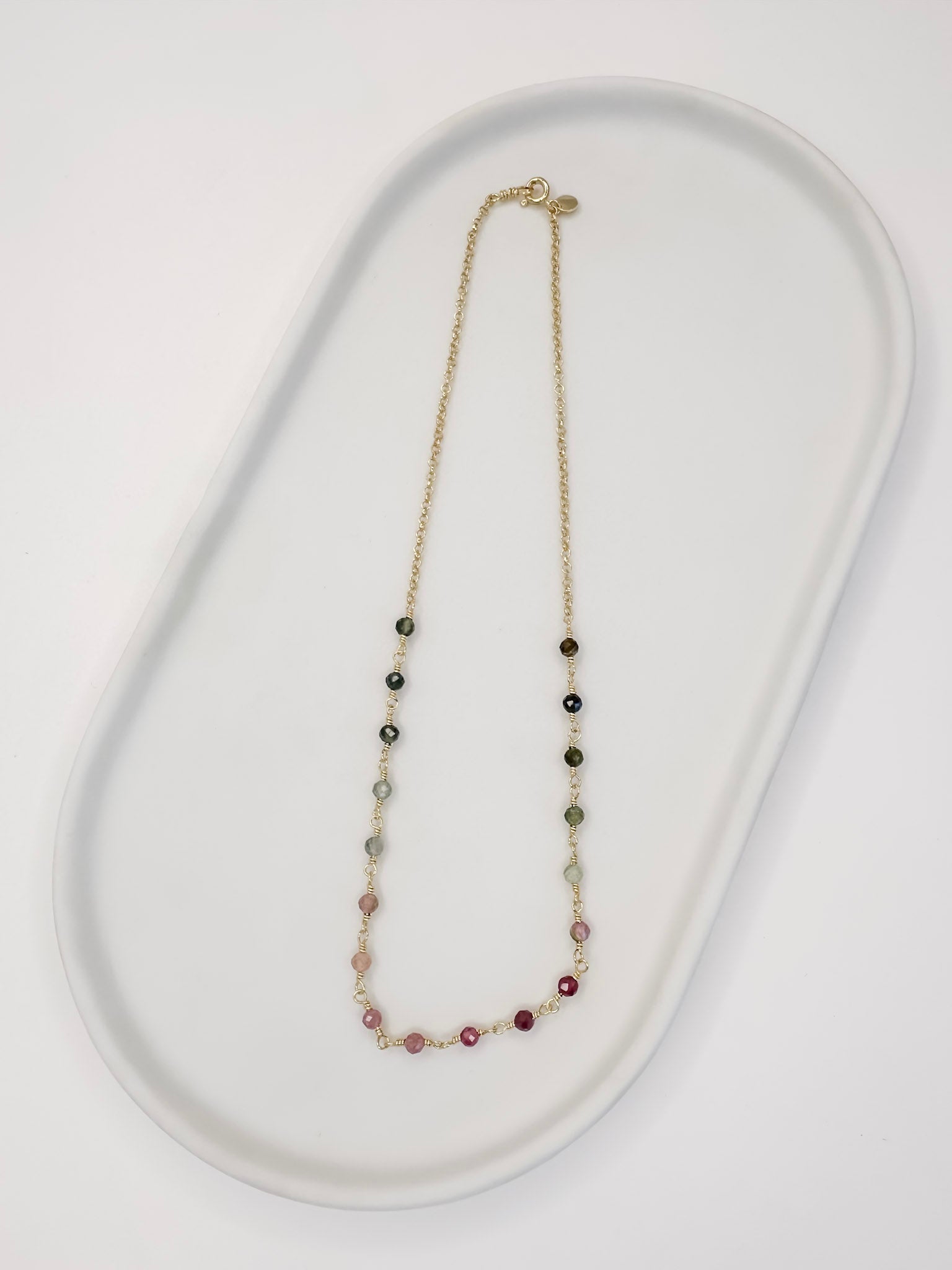 Colar tipo choker que também é Detalhe Pulseira de duas voltas de corrente portuguesa e turmaina melancia apoiada em uma bandeja branca com fundo branco.