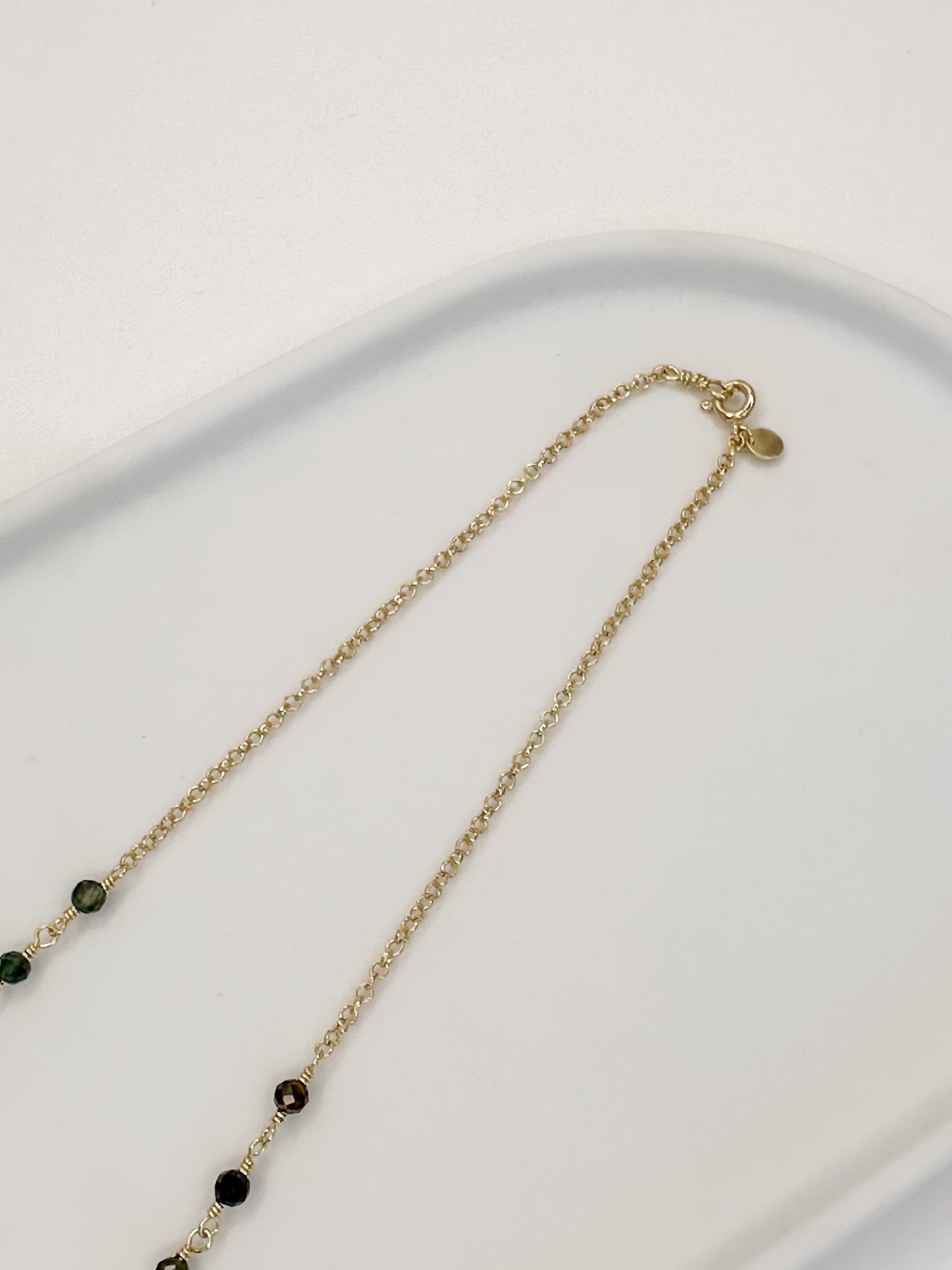 Colar tipo choker que também é Detalhe Fecho Boia Pulseira de duas voltas de corrente portuguesa e turmaina melancia apoiada em uma bandeja branca com fundo branco.