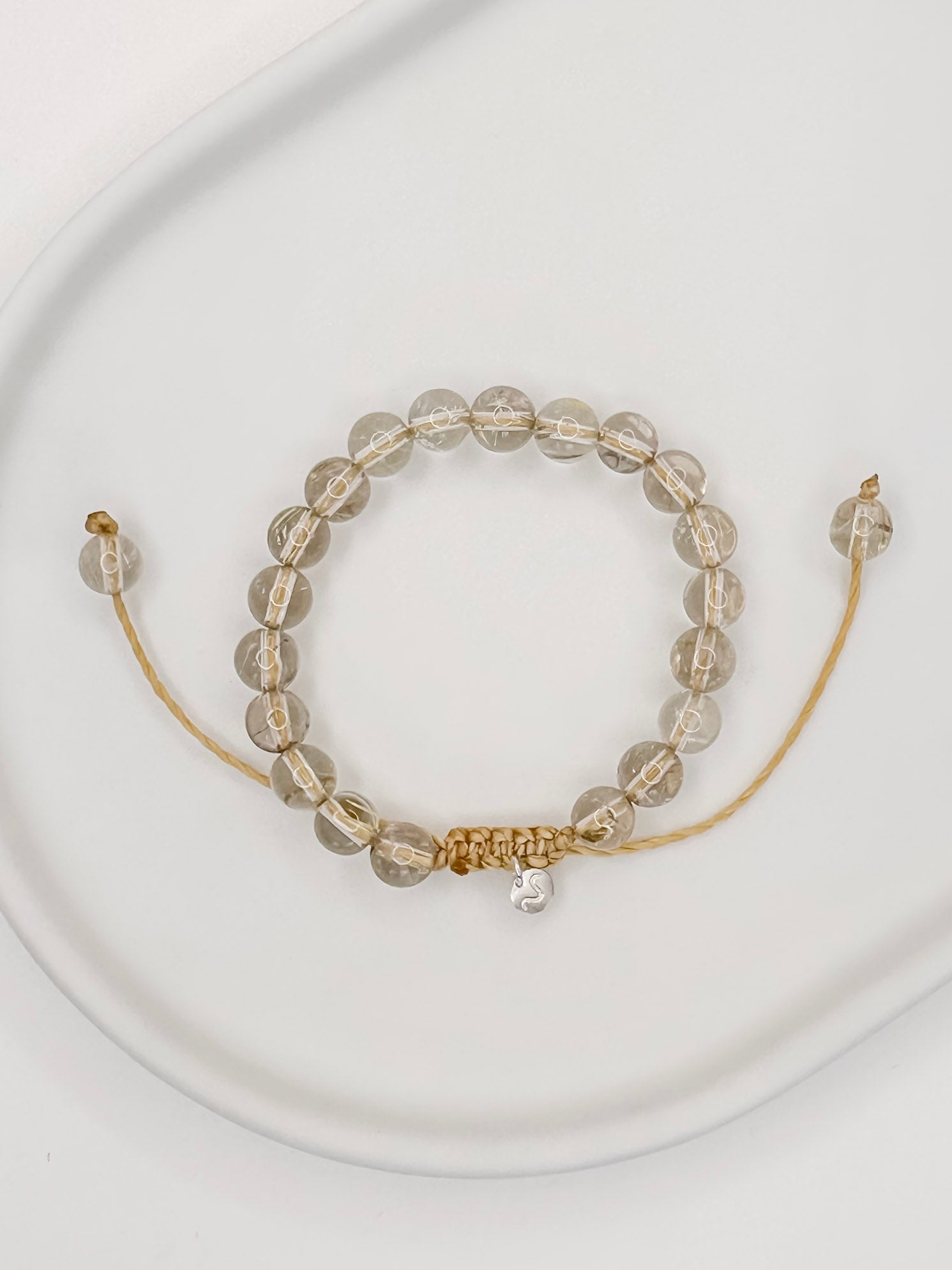 Pulseira de corda tamanho único com esferas de 6mm de quartzo rutilado natural apoiado em prato de cerâmica branco e fundo branco.
