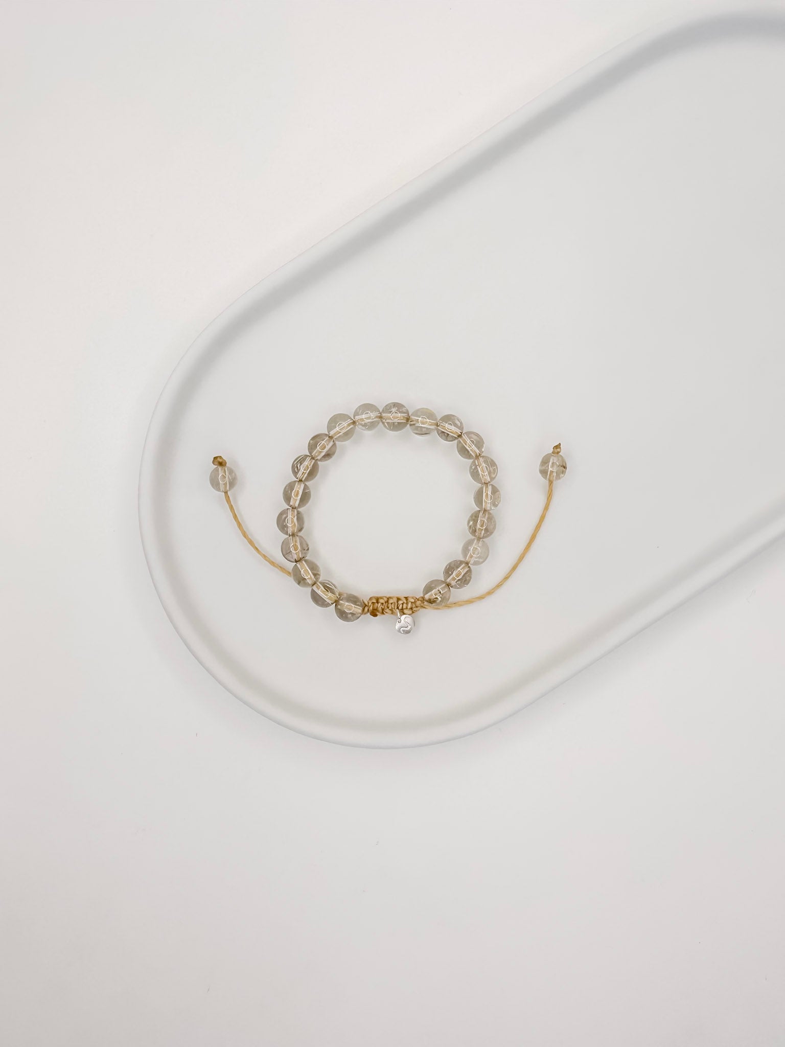 Pulseira de corda tamanho único com esferas de 6mm de quartzo rutilado natural apoiado em prato de cerâmica branco e fundo branco.