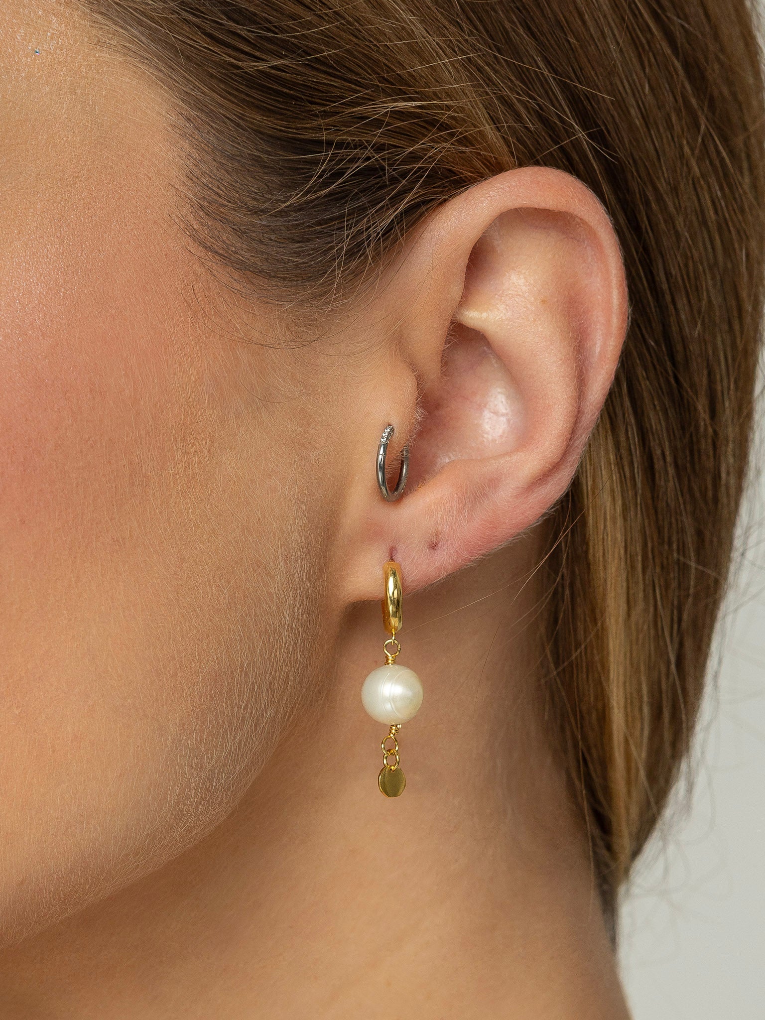 Brinco com uma mini argola em click e uma perola natural redonda pendurada e na ponta uma plaquinha redonda em prata 925 com banho de ouro 18k.