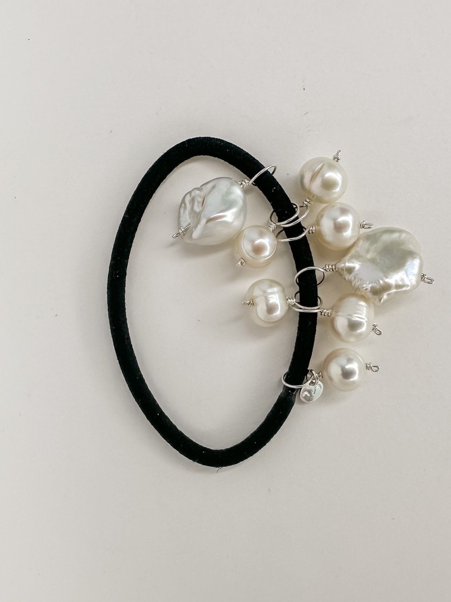 Elástico de cabelo preto pendurado com pérolas naturais de formatos diversos.