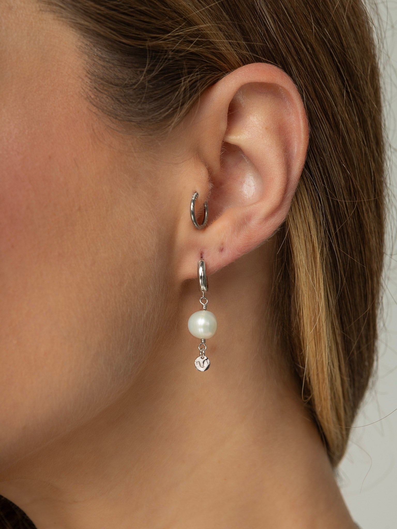 Brinco com uma mini argola em click e uma perola natural redonda pendurada e na ponta uma plaquinha redonda em prata 925 com banho de ródio branco (ouro branco).